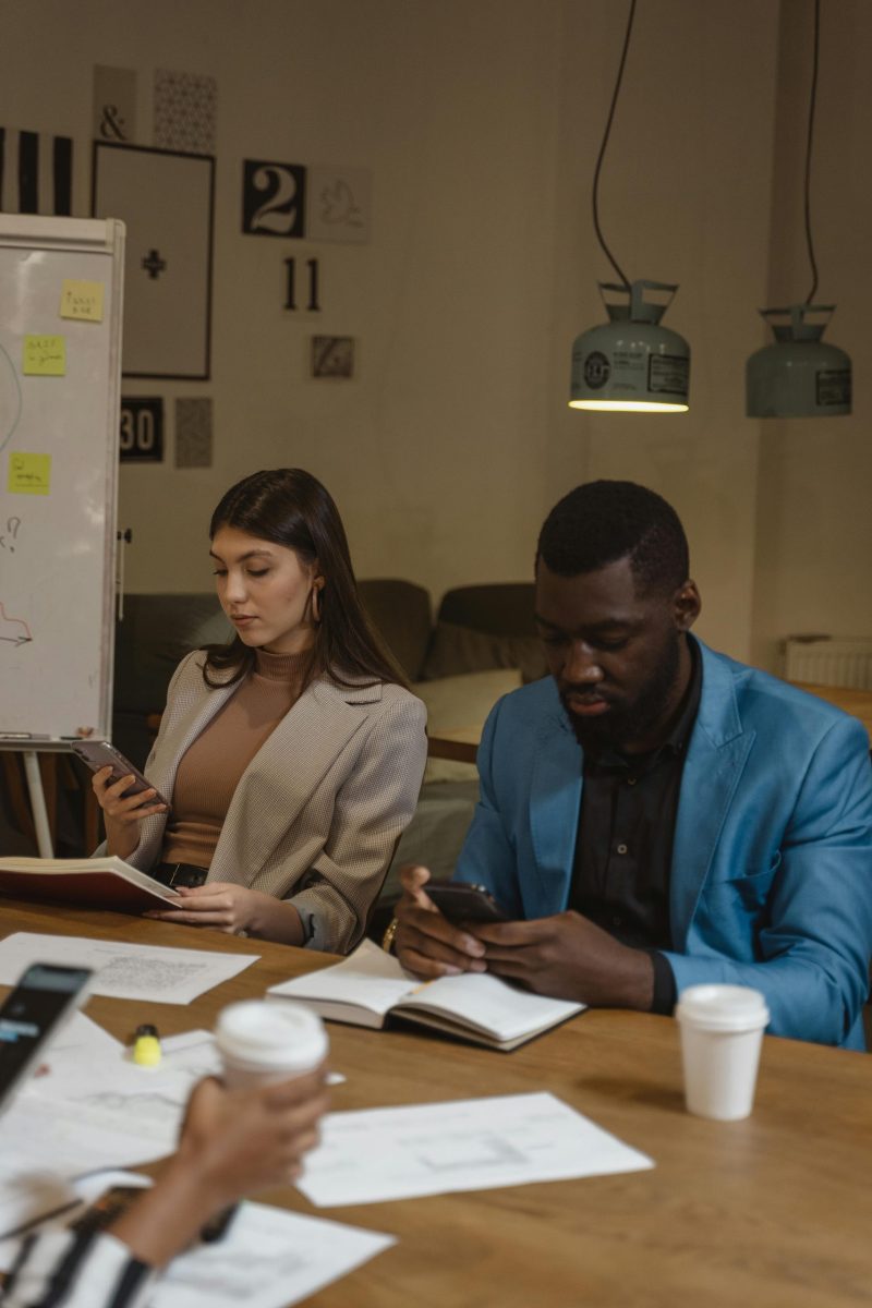 Diverse professionals collaborate in an office setting using smartphones and discussing work.